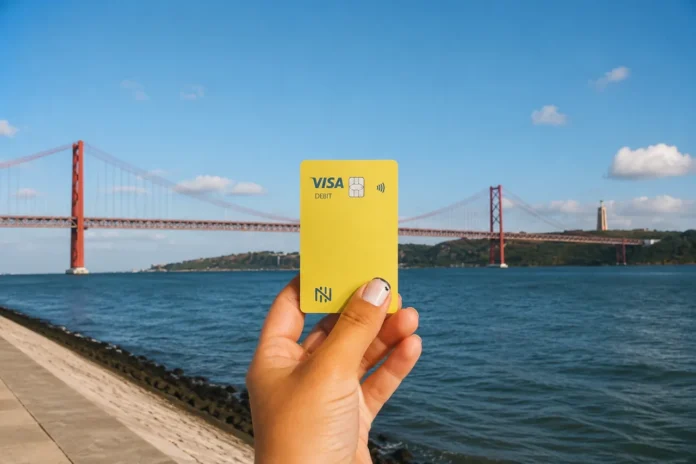 conta-nomad-euro-cartao-ponte-lisboa Cartão Visa da conta Nomad segurado em frente à ponte 25 de Abril, em Lisboa