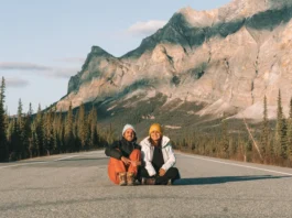 Dalton Highway: Tainá e Marcelo sentados no asfalto com a Sukakpak Mountain ao fundo, perto de Wiseman, no Alasca