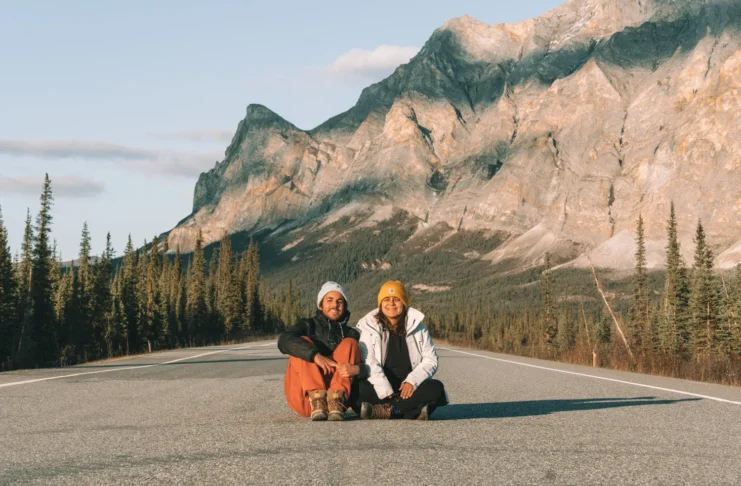 Dalton Highway: Tainá e Marcelo sentados no asfalto com a Sukakpak Mountain ao fundo, perto de Wiseman, no Alasca